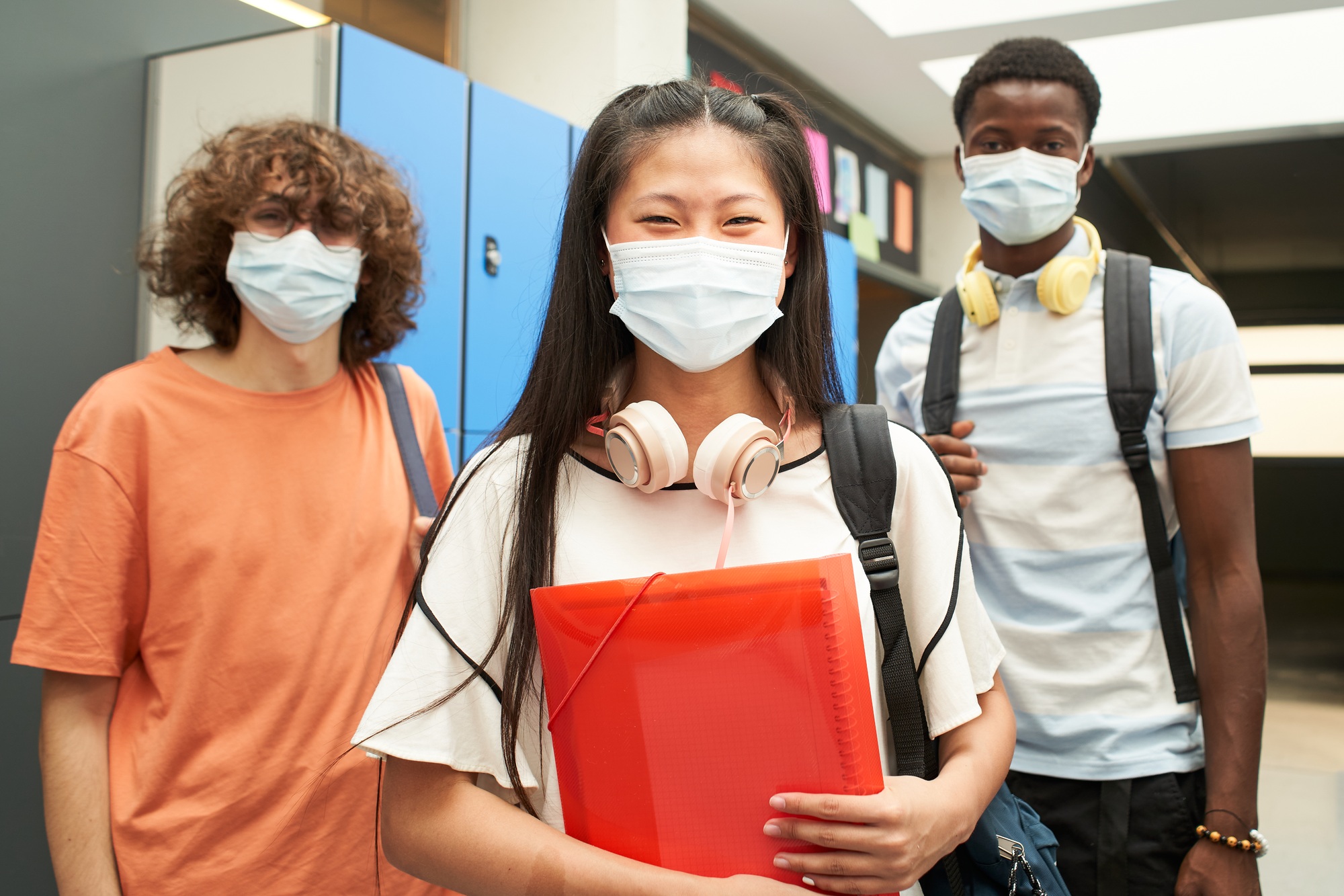 A group of multiracial students with mask looking at camera smiling. At school