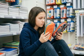 Adolescente comparant deux trousses scolaires colorées dans le rayon fournitures d'un supermarché
