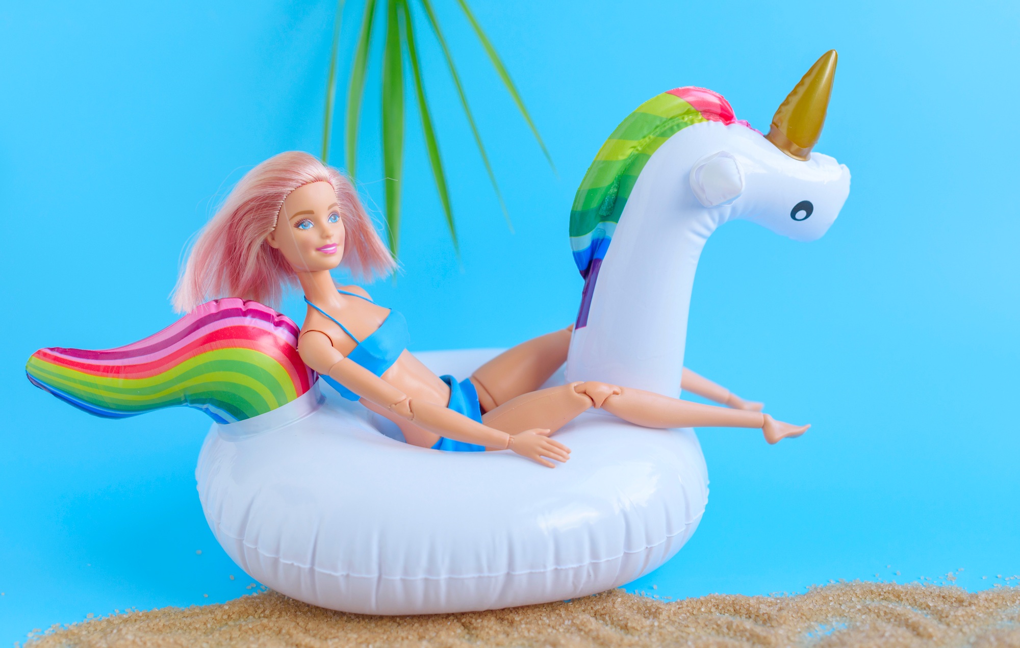 Barbie doll in swimsuit having rest on inflatable swan unicorn on the sea cost