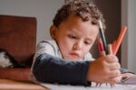 Child painting his drawing book with many colors. Boy discovering artistic talents