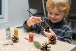 Christmas kids craft activities at home. Little child painting Christmas tree decorations.
