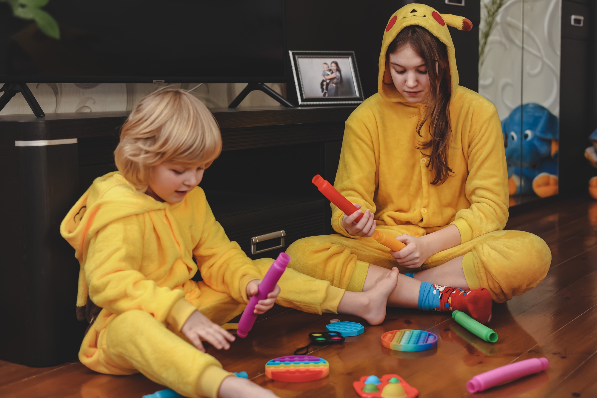 Cute children sister brother in trendy yellow Pikachu costumes playing with flexible tubes toys N