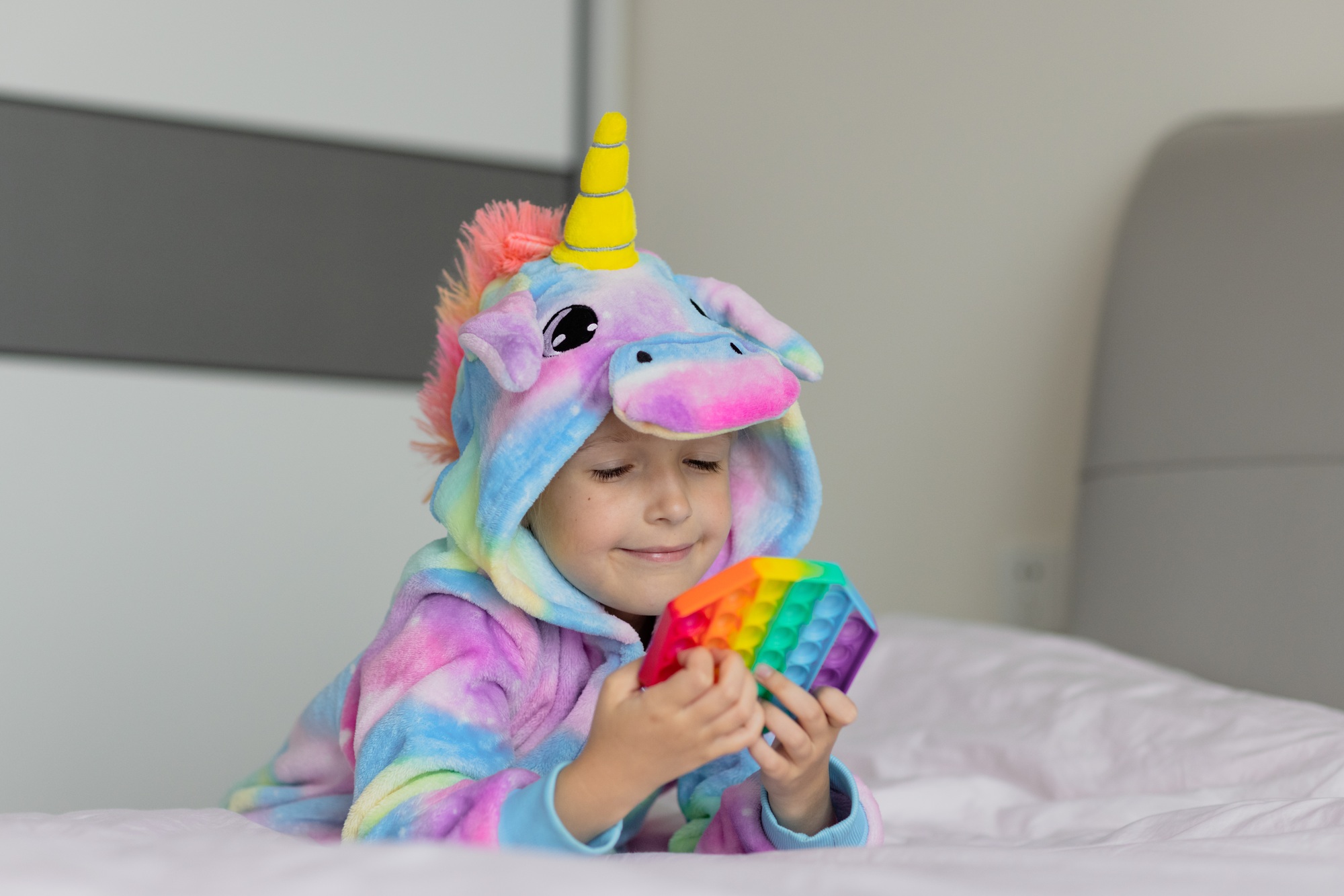 Cute little Caucasian girl with blonde hair wearing trendy bright and colorful unicorn kugurumi