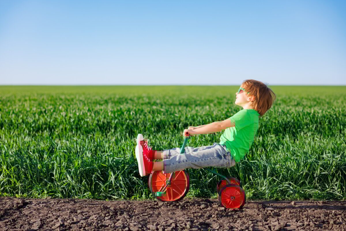 Happy child riding bike outdoor in spring green field