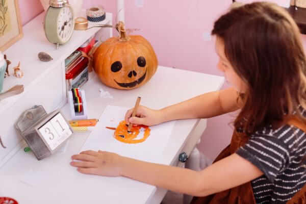 happy halloween. little girl draws a pumpkin and prepares to celebrate halloween at home