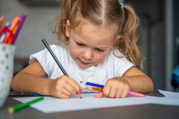 little girl draws with colored pencils in home.