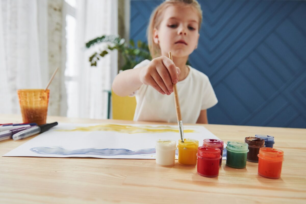 Takes the paint. Little girl is drawing by using gouache and brush. Learning in the art class