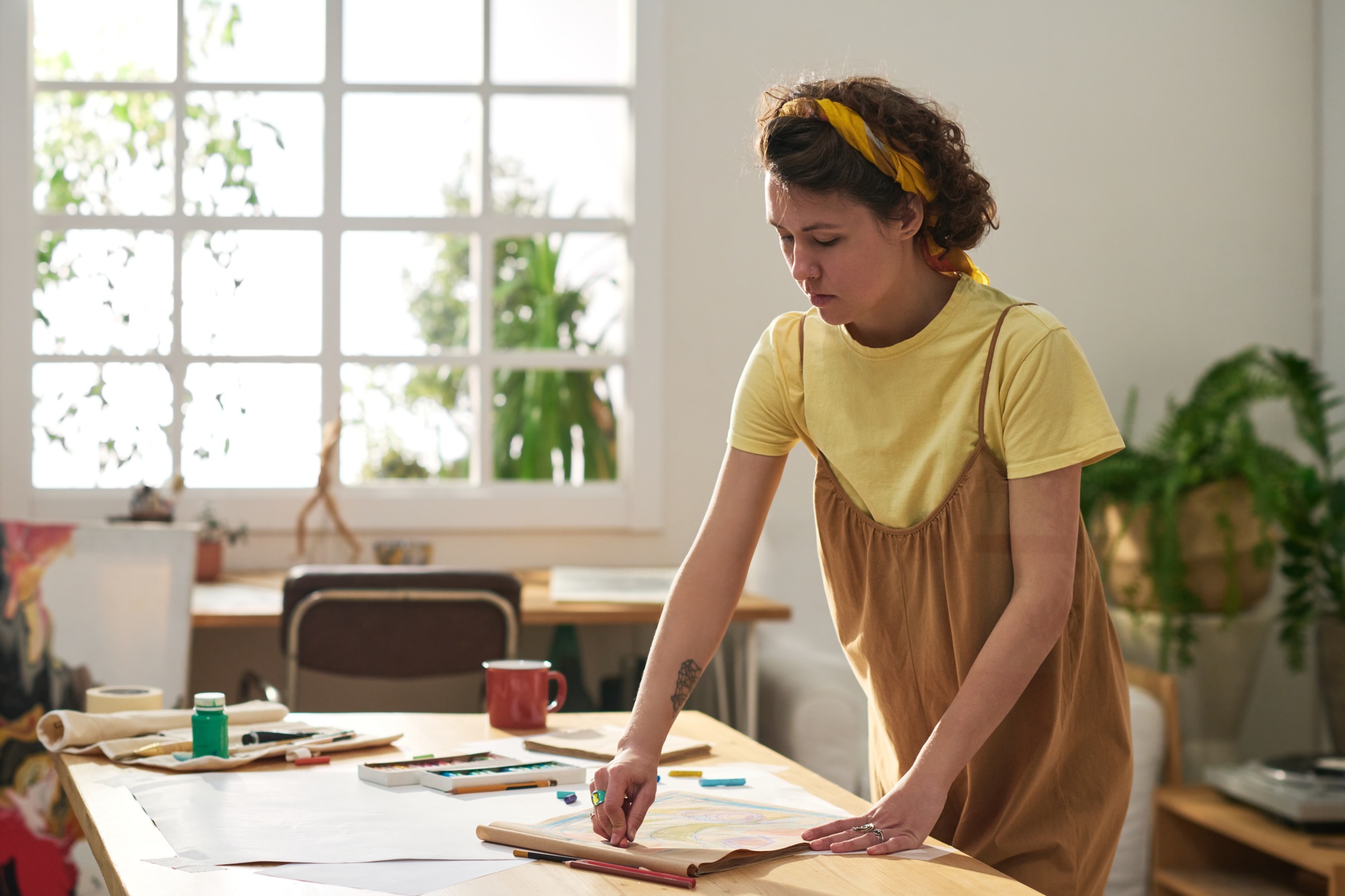 Young inspired craftswoman in casualwear standing by table and drawing